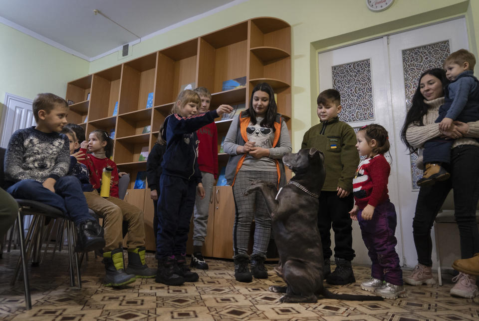 Children traumatized by the war play with an American Pit Bull Terrier "Bice" in the Center for Social and Psychological Rehabilitation in Boyarka close Kyiv, Ukraine, Wednesday, Dec. 7, 2022. Bice is an American pit bull terrier with an important and sensitive job in Ukraine — comforting children traumatized by the war. The Center for Social and Psychological Rehabilitation is a state-operated community center where a group of people are trying to help those who have experienced a trauma after the Feb. 24 Russian invasion, and now they are using dogs like Bice to give comfort. (AP Photo/Vasilisa Stepanenko)
