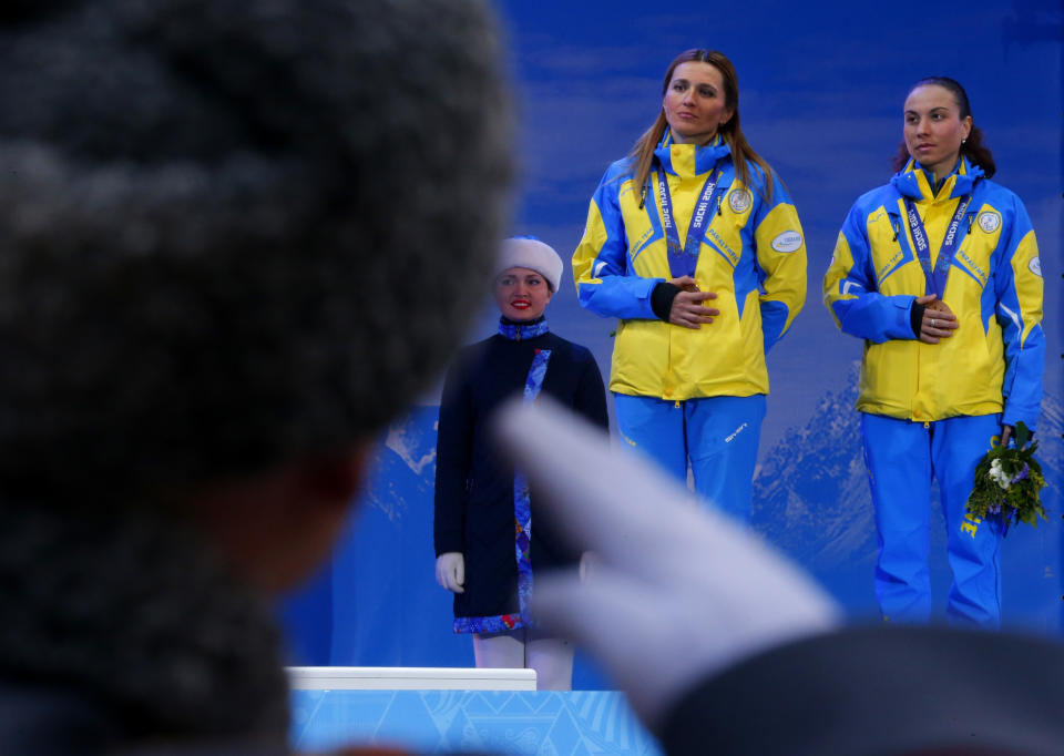 A Russian honor guard soldier salutes as Ukraine's Oksana Shyshkova , right, and her guide Lada Nesterenko cover their bronze medals with their hands after winning 3 place in the women's biathlon 12,5 km visually impaired event during a medal ceremony at the 2014 Winter Paralympic, Saturday, March 15, 2014, in Krasnaya Polyana, Russia. The majority of Ukraine's Paralympic medalists covered their medals during medal ceremonies. (AP Photo/Dmitry Lovetsky)