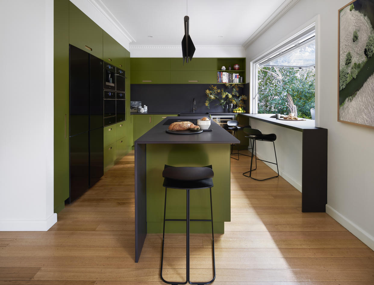  A dark green kitchen with black elements. 