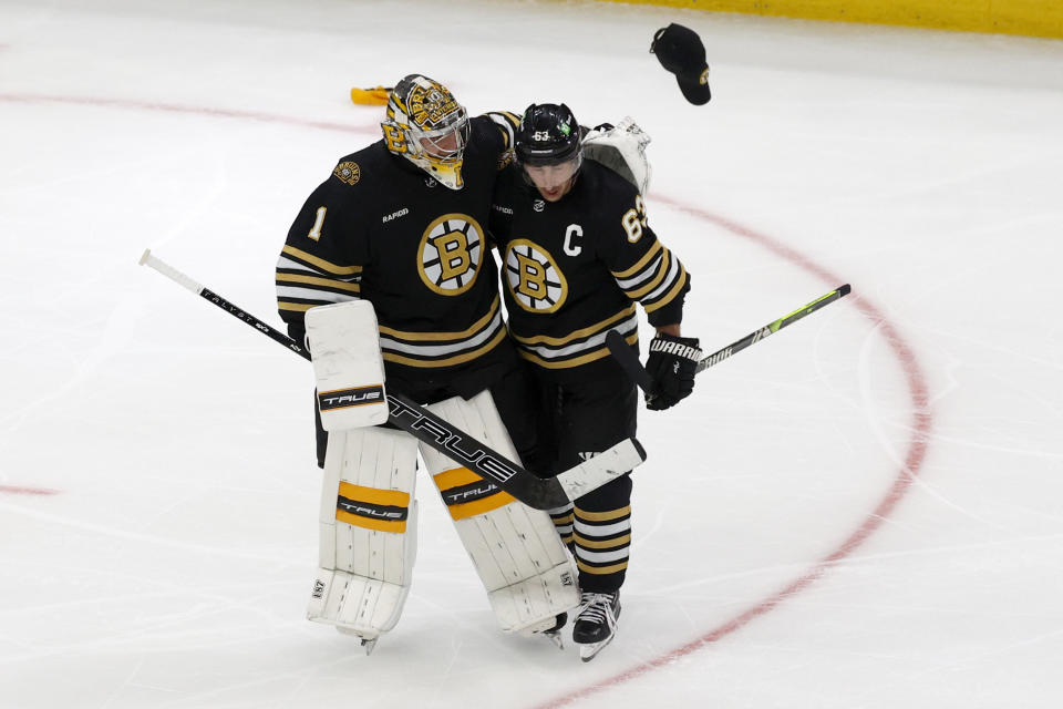 A cap is thrown onto the ice as Boston Bruins goalie Jeremy Swayman (1) congratulates teammate Brad Marchand (63) after Marchand scored his third goal for a hat trick during the third period of an NHL hockey game against the Columbus Blue Jackets, Sunday, Dec. 3, 2023, in Boston. (AP Photo/Mary Schwalm)