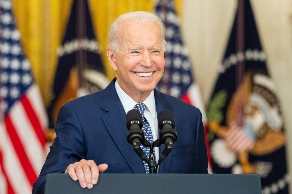 A smiling President Biden speaking with reporters in the East Room of the White House.