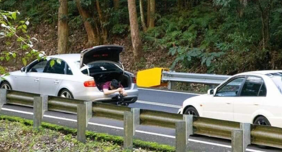 Pictured is the man holding a camera while hanging out of an Audi's boot in the Royal National Park near Sydney.