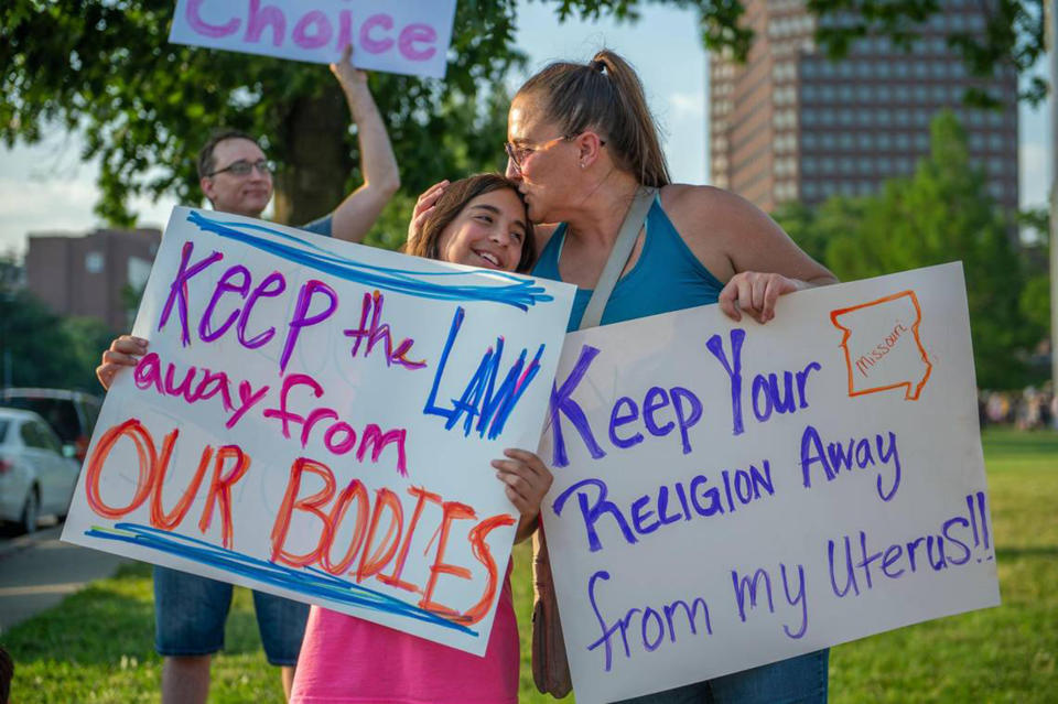 A girl and her mother hold signs reading: Keep the law away from our bodies and Keep your religion away from my uterus.