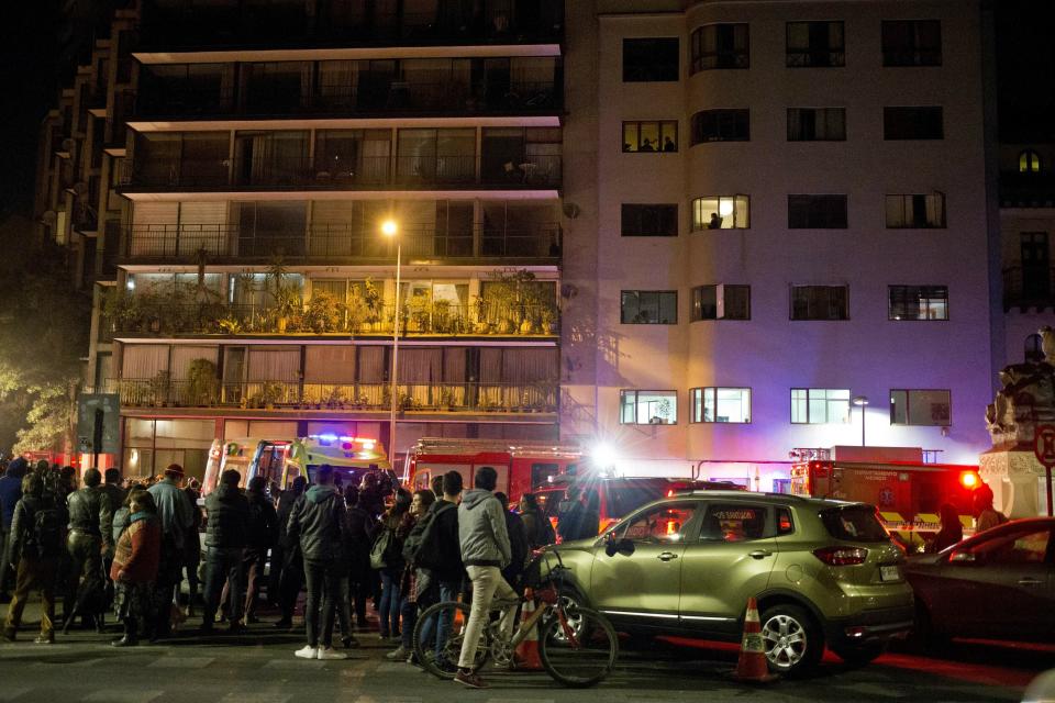 Onlookers look at the building where six Brazilians died in an apartment of apparent carbon monoxide poisoning in Santiago, Chile, Wednesday, May 22, 2019. Police commander Rodrigo Soto said officers found four adults and two children dead at the six-story building. The fire department said a high concentration of carbon monoxide was measured in the apartment, which it said was completely closed. (AP Photo/Esteban Felix)