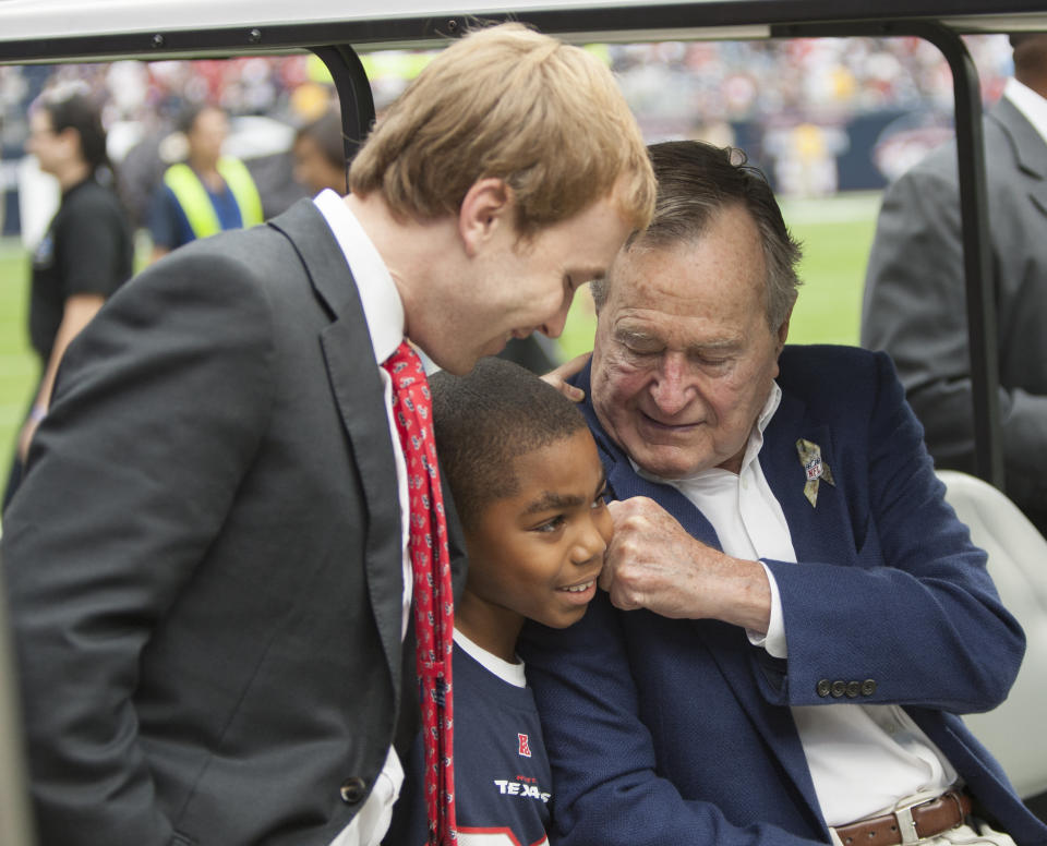 HOUSTON, TX - NOVEMBER 04:  Former President George H.W. Bush on hand playfully gives a young man a fist to his face as his grandson Pierce Bush looks on at Salute To Service day before the Houston Texans play the Buffalo Bills at Reliant Stadium on November 4, 2012 in Houston, Texas. (Photo by Bob Levey/Getty Images)