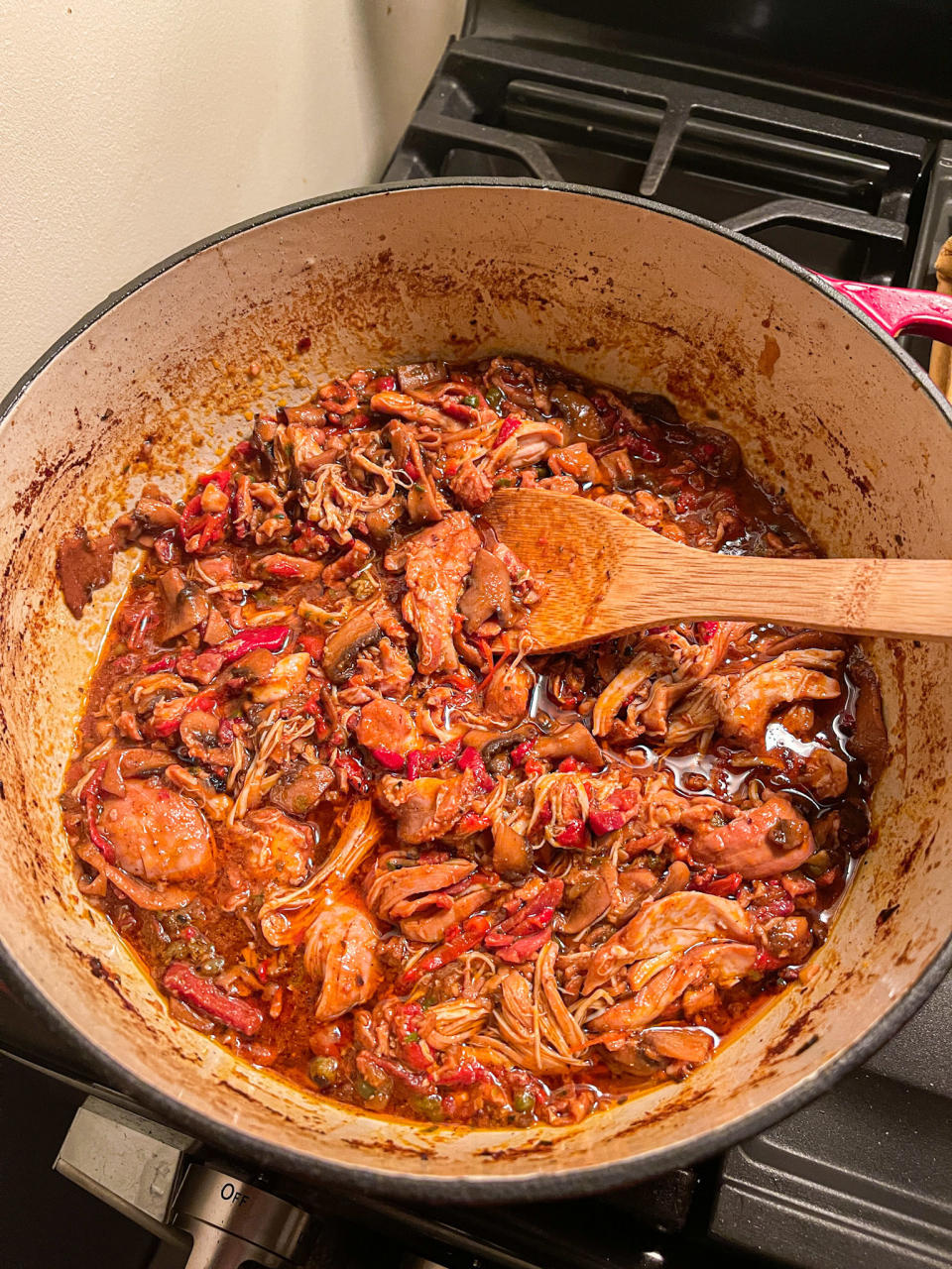 dutch oven with a deep red tomato sauce and shredded chicken, along with peppers and other veggies