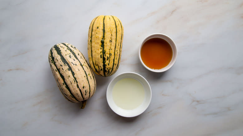 Whole squash next to oil and syrup in white bowls