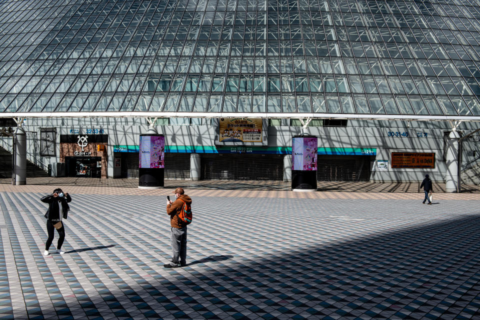 TOKYO, JAPAN - FEBRUARY 27: A couple wearing face masks take photographs outside the Tokyo Dome where a number of events including pop concerts have been cancelled because of concerns over the Covid-19 virus, on February 27, 2020 in Tokyo, Japan. A growing number of events and sporting fixtures are being cancelled or postponed around Japan while some businesses are asking their employees to work from home and some schools are closing as Covid-19 cases continue to increase and concerns mount over the possibility that the epidemic will force the postponement or even cancellation of the Tokyo Olympics. (Photo by Carl Court/Getty Images)