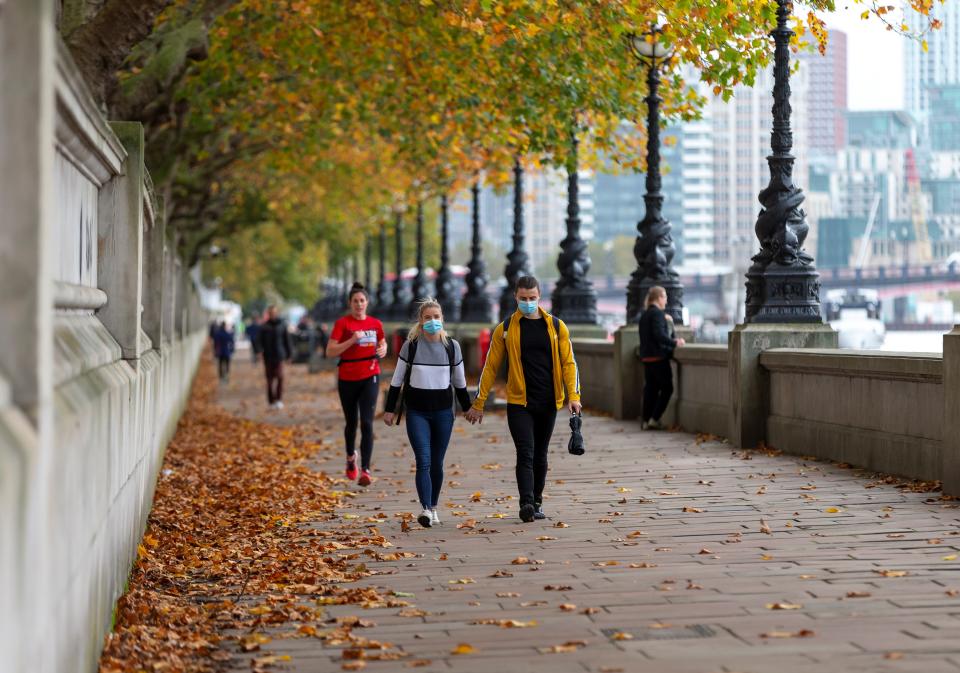 People wearing face masks walk by the River Thames in London, Britain, on Oct. 28, 2020