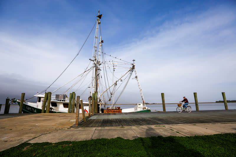 A man bicycles past the shrimp boat "Capt. T.J." owned by the 13 Mile Seafood company while it is docked in Apalachicola, Florida