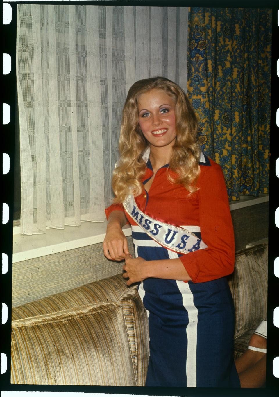 Miss USA 1974 Karen Jean Morrison poses in her sash near a window.