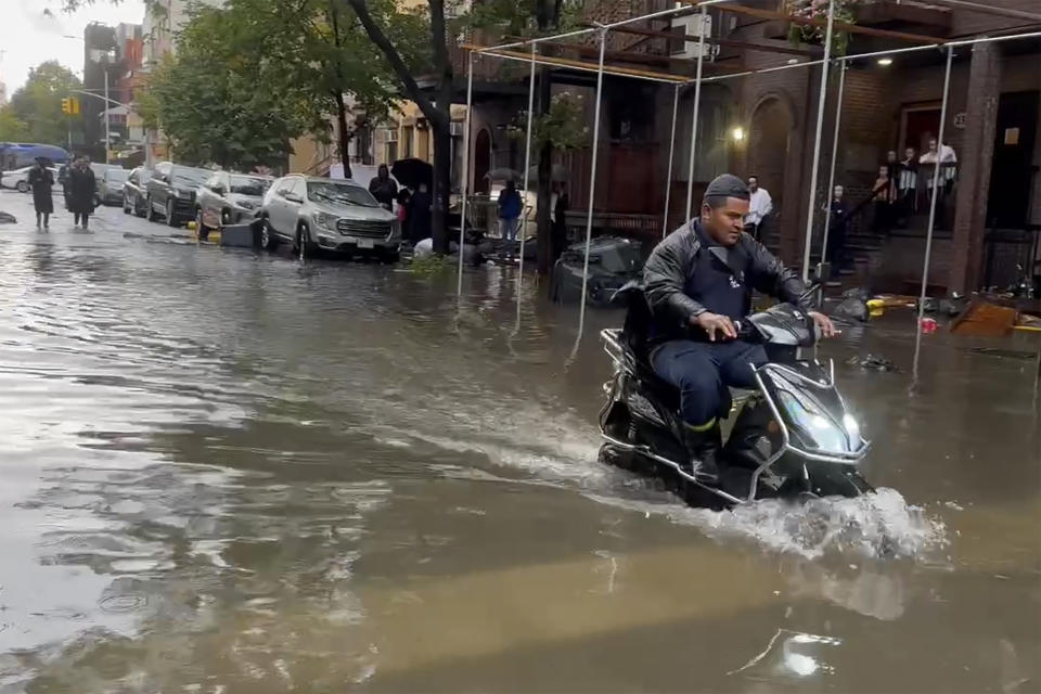 In this photo taken from video, a man drives a scooter through flood waters, Friday, Sept. 29, 2023, in the Brooklyn borough of New York. A potent rush-hour rainstorm has swamped the New York metropolitan area. The deluge Friday shut down swaths of the subway system, flooded some streets and highways, and cut off access to at least one terminal at LaGuardia Airport. (AP Photo/Jake Offenhartz)