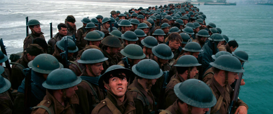 Myriad soldiers in helmets stand on a dock at sea as one soldier turns to look above