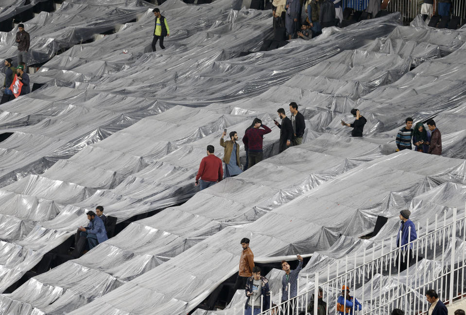 Spectators sit in an enclosure covered with plastic sheets during light rain fall while they wait for start of the Pakistan Super League T20 cricket match between Peshawar Zalmi and Lahore Qalandars at Rawalpindi stadium in Rawalpindi, Pakistan, Friday, Feb. 28, 2020. (AP Photo/Anjum Naveed)