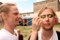 BERLIN, GERMANY - JULY 21: An attendee gets his face painted with glitter at the second annual Hipster Olympics on July 21, 2012 in Berlin, Germany. With events such as the "Horn-Rimmed Glasses Throw," "Skinny Jeans Tug-O-War," "Vinyl Record Spinning Contest" and "Cloth Tote Sack Race," the Hipster Olympics both mocks and celebrates the Hipster subculture, which some critics claim could never be accurately defined and others that it never existed in the first place. The imprecise nature of determining what makes one a member means that the symptomatic elements of adherants to the group vary in each country, but the archetype of the version in Berlin, one of the more popular locations for those following its lifestyle, along with London and Brooklyn, includes a penchant for canvas tote bags, the carbonated yerba mate drink Club Mate, analogue film cameras, an asymetrical haircut, 80s neon fashion, and, allegedly, a heavy dose of irony. To some in Berlin, members of the hipster "movement" have replaced a former unwanted identity in gentrifying neighborhoods, the Yuppie, for targets of criticism, as landlords raise rents in the areas to which they relocate, particularly the up-and-coming neighborhood of Neukoelln. (Photo by Adam Berry/Getty Images)