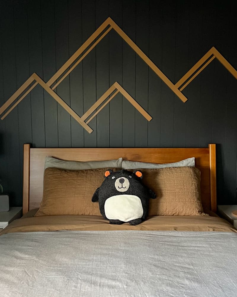 Neatly made bed in child's room with black painted walls.