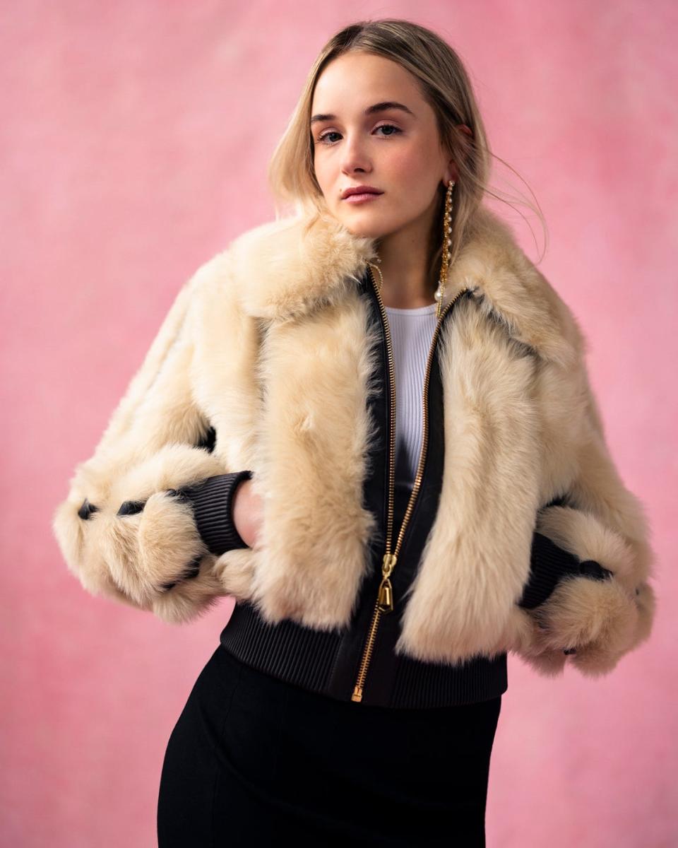 actress miriam petche from industry season 3 wearing a furry coat standing in front of a pink backdrop