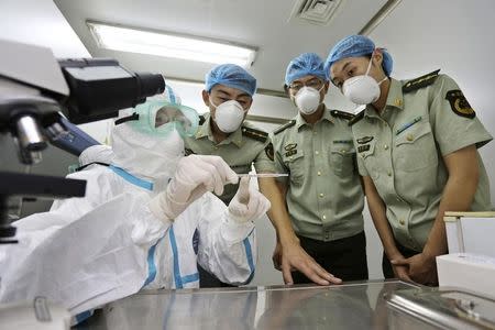 A health inspection and quarantine researcher (L) demonstrates to customs policemen the symptoms of Ebola, at a laboratory at an airport in Qingdao, Shandong province August 11, 2014. REUTERS/China Daily