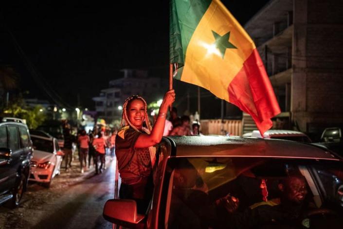 A woman leans out a car window and waves the Senegalese flag.