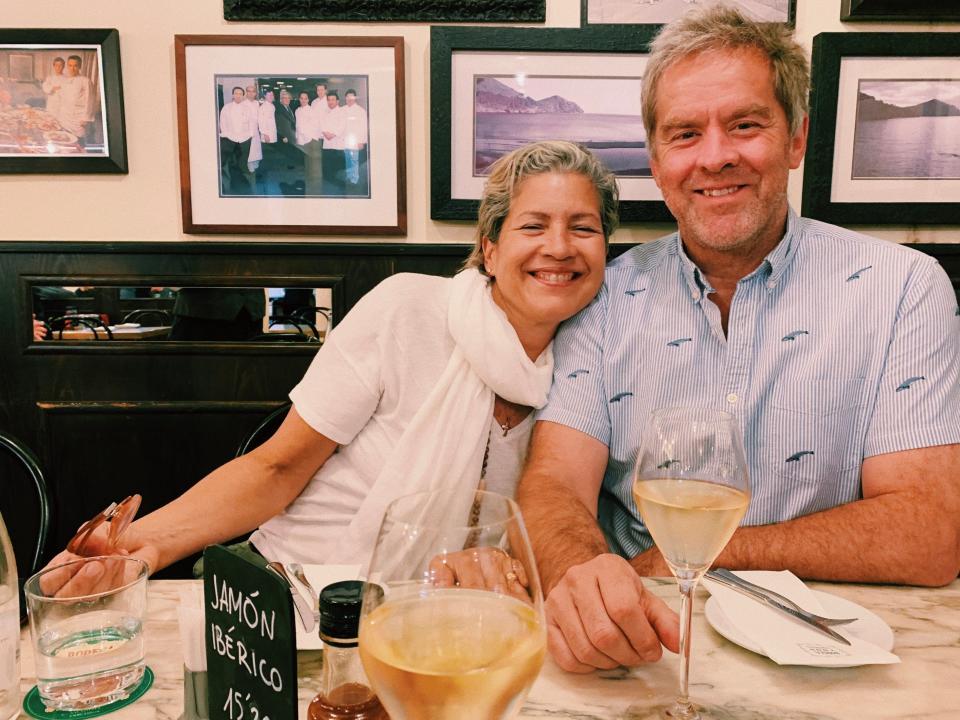 Maria Isabel Melendez, a Latina woman, and Bob Noyen, a white man, both in their 50s, smile with a glass of wine at a restaurant table.