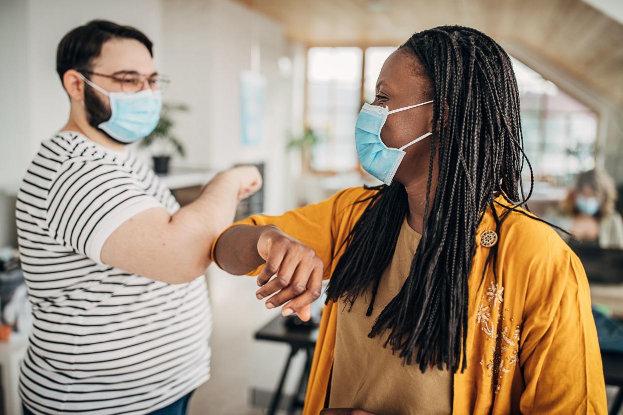 Two people, business team working with protective masks together in modern office, man and woman greeting with elbows.