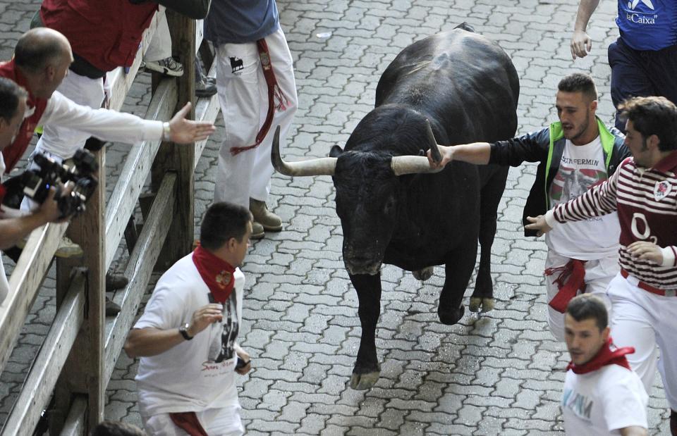 A spectator on the barrier (L) calls a participant out for grabbing the horn of a Victoriano del Rio Cortes' bull during the third 'encierro' (bull-run) of the San Fermin Festival in Pamplona, northern Spain, on July 9, 2015. The festival is a symbol of Spanish culture that attracts thousands of tourists to watch the bull runs despite heavy condemnation from animal rights groups. AFP PHOTO/ ANDER GILLENEA        (Photo credit should read ANDER GILLENEA/AFP/Getty Images)