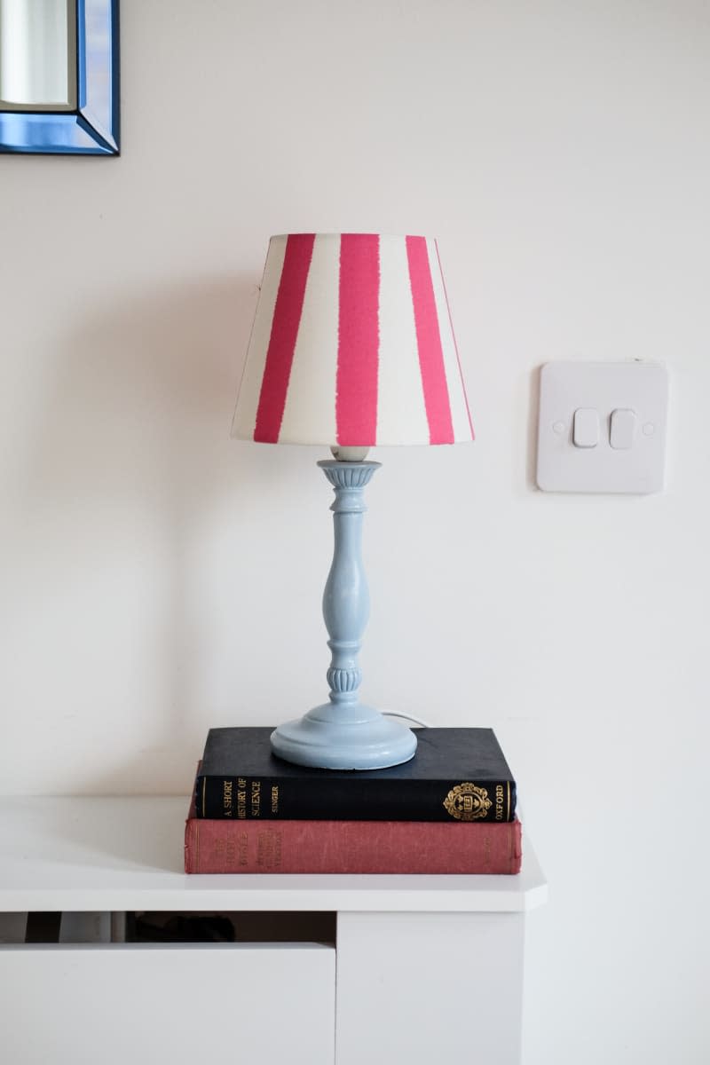 pink and white striped lamp shade with light blue base on top of two books on white table