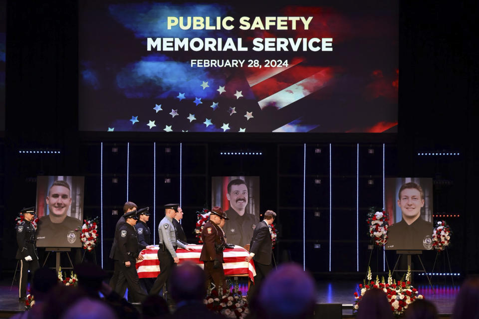 FILE - The caskets representing the fallen are brought into the sanctuary at Grace Church before the start of the memorial service there for Burnsville police officer Paul Elmstrand, whose picture stands at left; firefighter-paramedic Adam Finseth, whose picture stands center; and and police officer Matthew Ruge, whose picture stands at right, in Eden Prairie, Minn., Feb. 28, 2024. A woman has been charged with illegally buying guns used in the killings of the three Minnesota first responders in a standoff at a home in Burnsville, where seven children were inside, U.S. Attorney Andrew M. Luger announced Thursday, March 14, at a news conference. (Aaron Lavinsky/Star Tribune via AP, Pool, File)