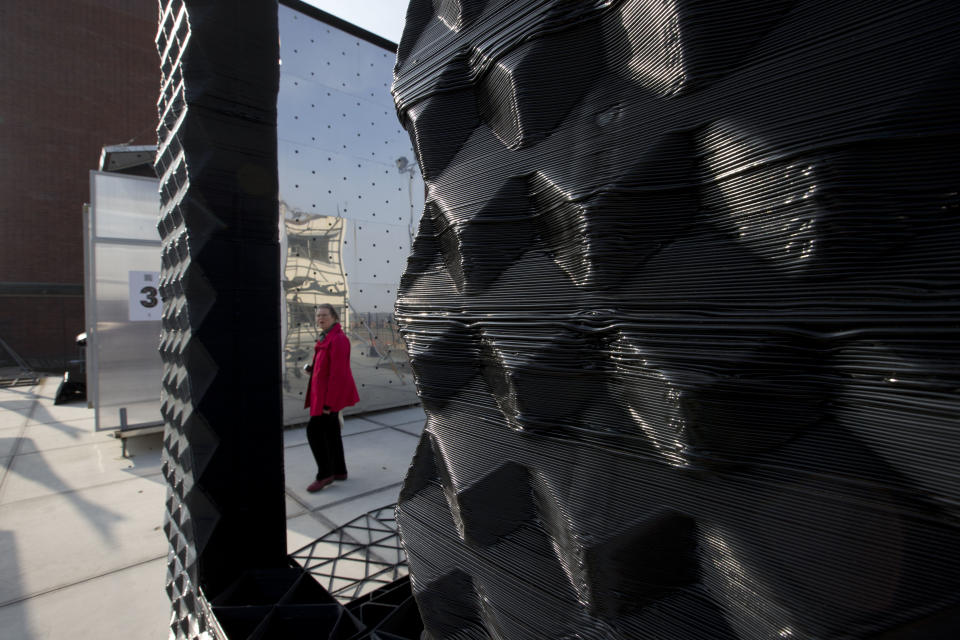 A visitor passes a 3D printer, rear, as she looks at part of a printed canal house, foreground, in Amsterdam, Netherlands, Thursday, March 13, 2014. Dutch architecture firm Dus has embarked on a project to build a 21st-century version of a classic Amsterdam canal house, printing it out piece by piece with an oversized 3-D printer, and then slotting them together like oversized Lego blocks. The goal is to discover and share the potential uses of 3-D printing in construction by creating new materials, trying out designs and testing building techniques. (AP Photo/Peter Dejong)