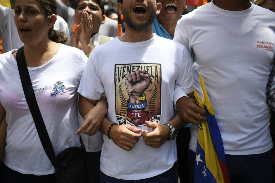 A man wearing a shirt that reads in Spanish "Venezuela. Strength and faith." links arms with others at an opposition rally in Caracas, Venezuela, Tuesday, March 10, 2020. U.S.-backed Venezuelan political leader Juan Guaido will lead a march aimed at retaking the National Assembly legislative building, which opposition lawmakers have been blocked from entering. (AP Photo/Matias Delacroix)