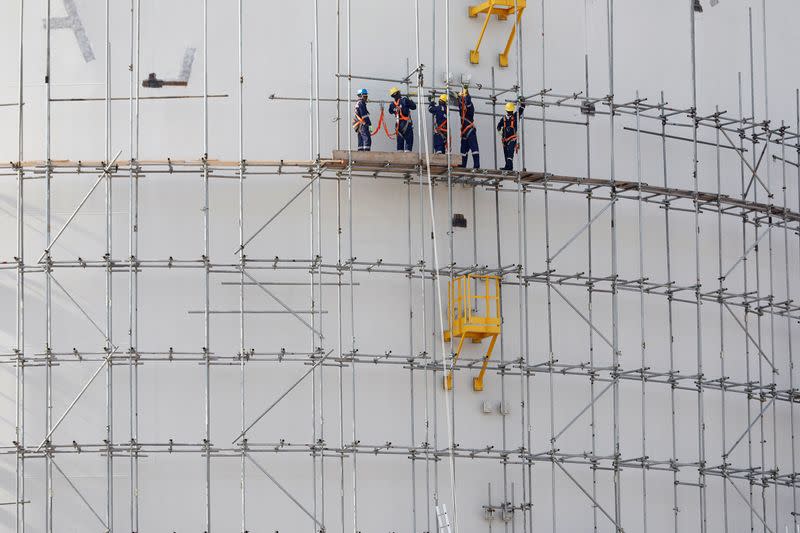 FILE PHOTO: Construction workers are seen standing on a scaffolding on a oil tank at the Dangote Refinery under construction in Ibeju Lekki district, on the outskirts of Lagos