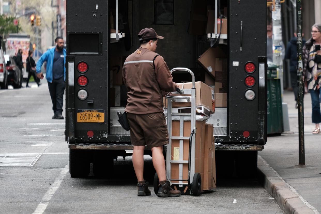 UPS driver stands behind his truck with packages on a dolly.