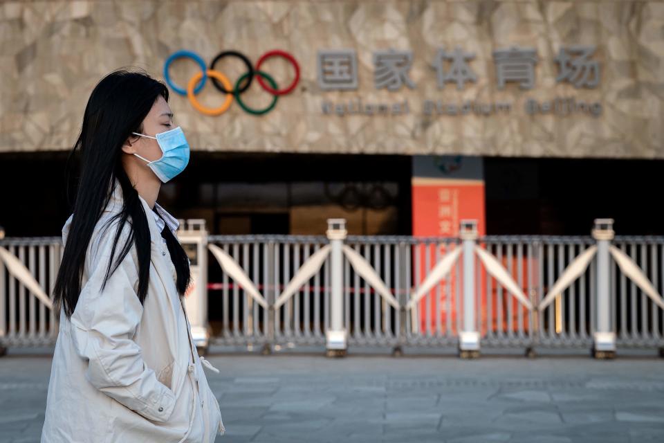 A woman wearing a facemask as a preventive measure against the COVID-19 novel coronavirus walks at the Olympic park in Beijing on March 23, 2020. - World Athletics chief Sebastian Coe has called for the Tokyo Olympics to be postponed over the coronavirus pandemic as Canada pulled out of the Games and Japan's prime minister admitted a delay could be "inevitable". (Photo by Nicolas ASFOURI / AFP) (Photo by NICOLAS ASFOURI/AFP via Getty Images)