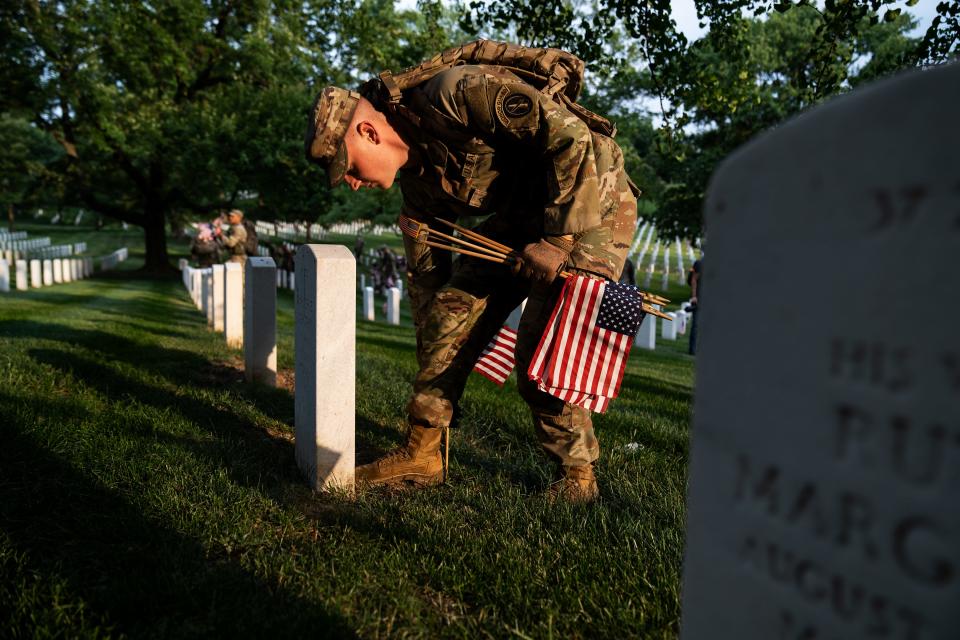 A member of the 3rd U.S. Infantry Regiment places a flag into the ground, exactly one boot length from the headstone's base during a joint service “Flags-In” ceremony at Arlington National Cemetery on Thursday, May 25, 2023.