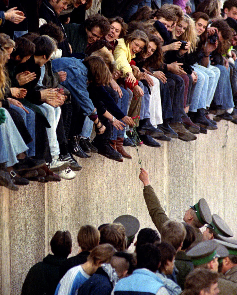 An East Berlin border guard hands a flower back to West Berlin citizens who are sitting atop the Berlin Wall in front of the Brandenburg Gate. Other West Berlin citizens mingle with border guards on the East Berlin side on Nov. 9, 1989. (Photo: Reuters)