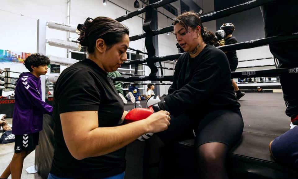 Gym mom Jessica Bautista, left, takes off hand wraps for Perla Nera after her sparring session at the Diamond Hill Community Center in Fort Worth.