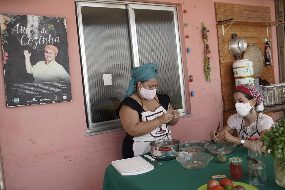 La chef Regina Tchelly (de pie) y la activista Marisa Furtado pelan semillas de yaca en el proyecto culinario Favela Orgánica que dirige Tchelly en la favela Babilonia de Río de Janeiro el 11 de febrero del 2021. (AP Photo/Silvia Izquierdo)