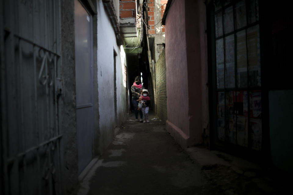 En esta imagen, tomada el 29 de mayo de 2020, una niña con una muñeca en brazos, acompañada de una mujer adulta, camina por un callejón de villa 1-11-14 durante la cuarentena ordenada por el gobierno para frenar la propagación del nuevo coronavirus, en Buenos Aires, Argentina. (AP Foto/Natacha Pisarenko)