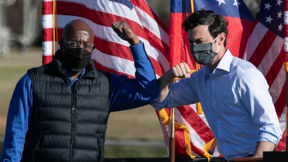 Democratic U.S. Senate candidates Raphael Warnock (left) and Jon Ossoff bump elbows during a Dec. 5 outdoor drive-in rally in Conyers, Georgia. (Photo by Jessica McGowan/Getty Images)