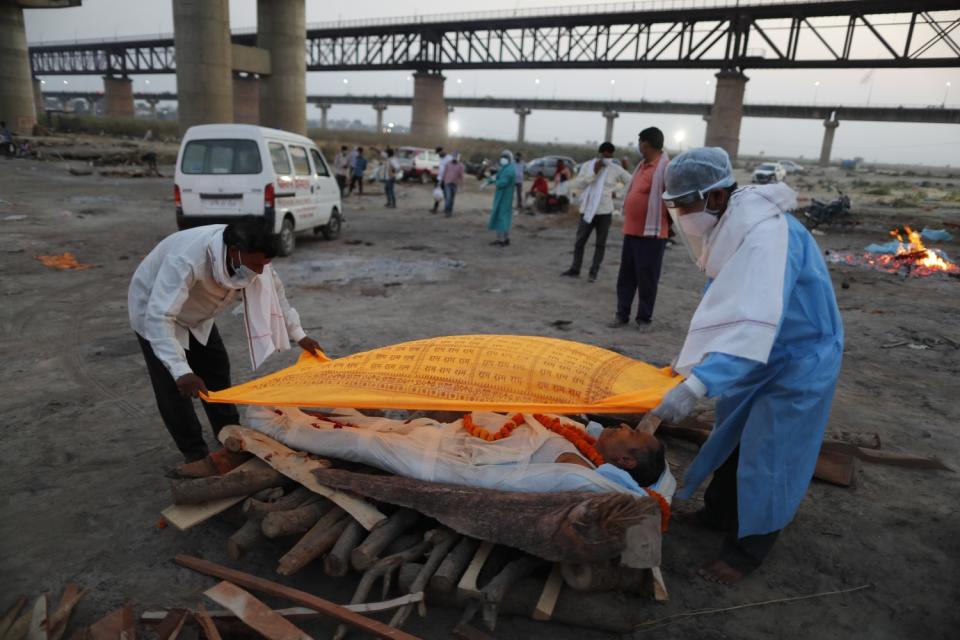 Two people place a patterned orange cloth over a body lying atop a pile of logs