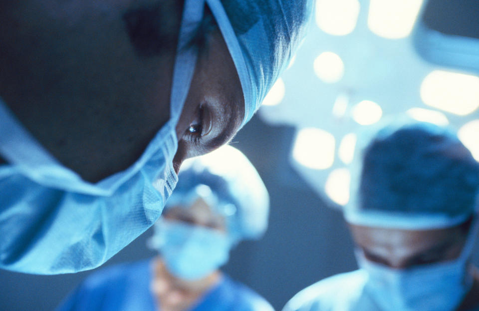 Surgeons focus intently on a medical procedure in a well-lit operating room, wearing surgical masks and caps