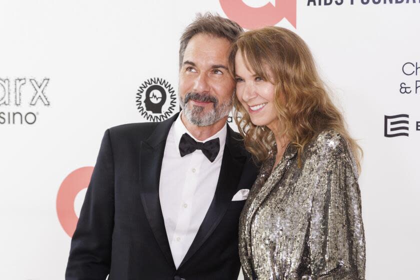 Eric McCormack in a suit smiles next to Janet McCormack in a silver sequined dress as they pose together