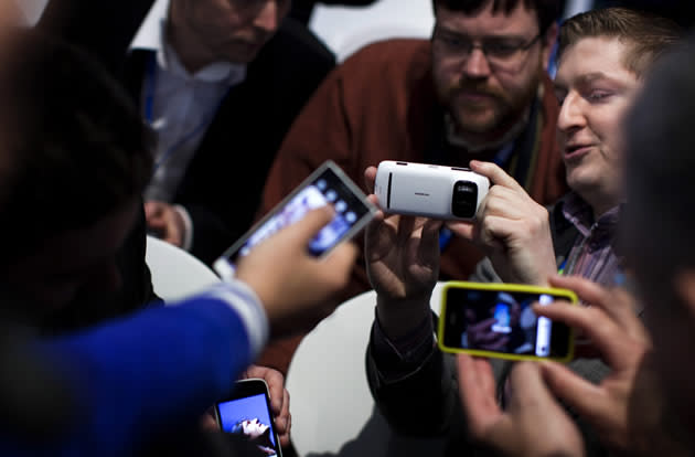 A worker of Nokia Corporation, right, holds a new model of his mobile phone company as visitors take photos with their mobile phones.