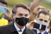 Brazil's President Jair Bolsonaro, wearing a face mask amid the new coronavirus pandemic, stands amid supporters taking pictures with cell phones as he leaves his official residence of Alvorada palace in Brasilia, Brazil, Monday, May 25, 2020. (AP Photo/Eraldo Peres)