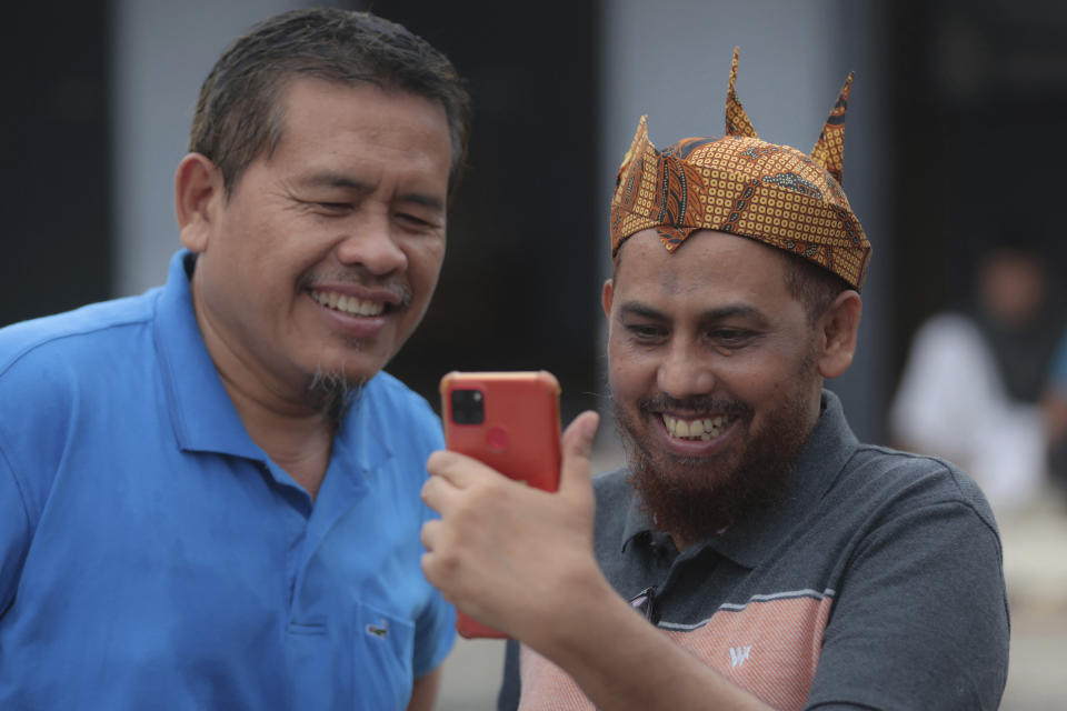 Indonesian militant Umar Patek, right, uses his mobile phone to make a video call as his long-time friend Ali Fauzi, a former bomb maker for who now runs a program aimed at de-radicalizing militants, joins during their meeting in Lamongan, East Java, Indonesia, Tuesday, Dec. 13, 2022. Patek, who was convicted of making the explosives used in the attack that killed over 200 people, was paroled last week after serving about half of his original 20-year prison sentence. (AP Photo/Trisnadi)
