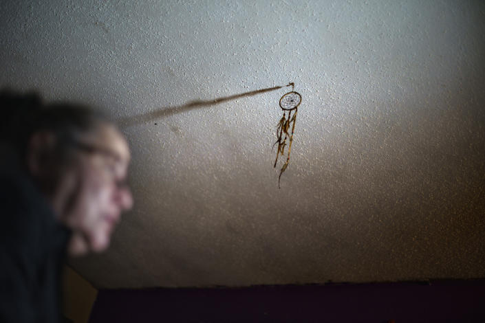 A dreamcatcher hangs from the ceiling above Betty Oppegard, whose daughter, Beth Renee Hill, died of an overdose, as she sits in her home Thursday, Nov. 18, 2021, in Naytahwaush, Minn. Despite their resilience, Native Americans carry in their blood 500 years of trauma, accumulating from one generation to the next, from being robbed of their land, their language, their culture, their children. Hill's grandmother was sent to a boarding school, where they cut her hair and forbid her language. "That's always a part of you when you're born native," said Oppegard. (AP Photo/David Goldman)