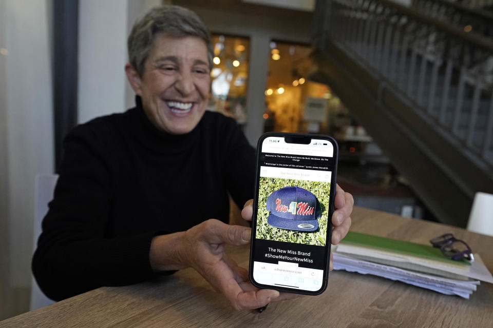 Suzi Altman holds a cell phone photograph of the "New Miss" hat, Nov. 23, 2021, in Jackson, Miss. The hat and shirts she produces, uses the same the cursive script as the Ole Miss logo that appears on football helmets, sports jerseys, marketing materials and all manner of bags, clothing and other merchandise licensed by the University of Mississippi. Altman applied for the New Miss trademark in July 2020, but the school has filed papers trying to block her from trademarking the "New Miss" logo. (AP Photo/Rogelio V. Solis)