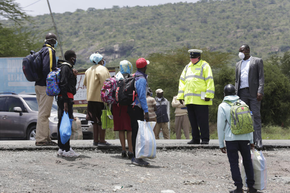 A Kenyan police officer speaks to people at a road block along Mombasa Road after vehicles traveling to Mombasa and Machakos were turned away, in Nairobi, Kenya, Tuesday, April 7, 2020. Kenya increased its restrictions to combat the coronavirus, announcing travel bans into and out of the capital city, Nairobi, the port of Mombasa and two counties. More than half of Africa’s 54 countries have imposed lockdowns, curfews, travel bans or other restrictions to try to contain the spread of COVID-19. (AP Photo/Khalil Senosi)