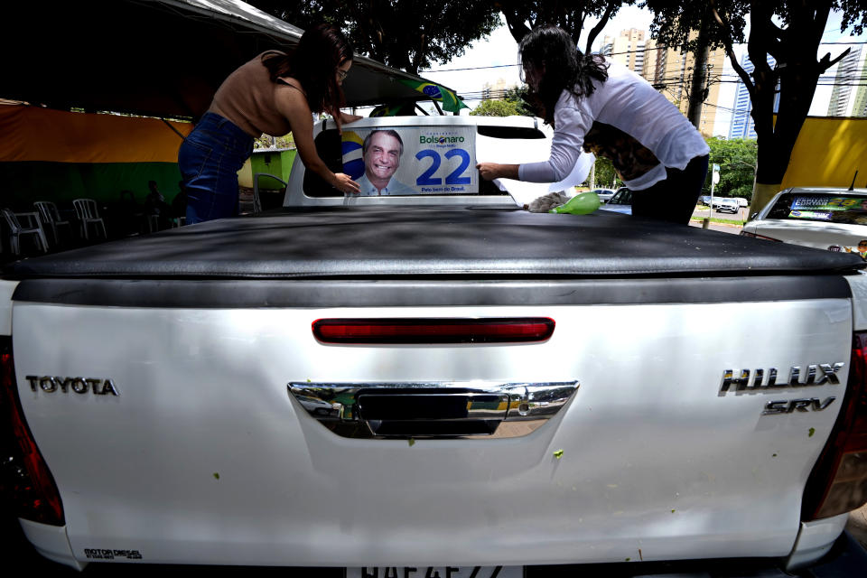 Supporters of Brazilian President Jair Bolsonaro place an electoral photo of the president on a truck at a local campaign headquarters where Bolsonaro supporters can get free swag in Campo Grande, Mato Grosso state, Brazil, Friday, Oct. 21, 2022. The presidential run-off election is set for Oct. 30. (AP Photo/Eraldo Peres)