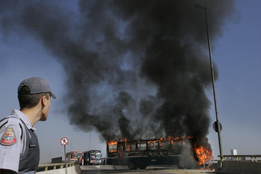 A policeman looks at a municipal bus set on fire in São Paulo, Brazil, on 22 July 2006 amid a string of PCC-linked attacks.